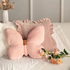Pink butterfly-shaped pillow on a bed with flowers and a vase in the background