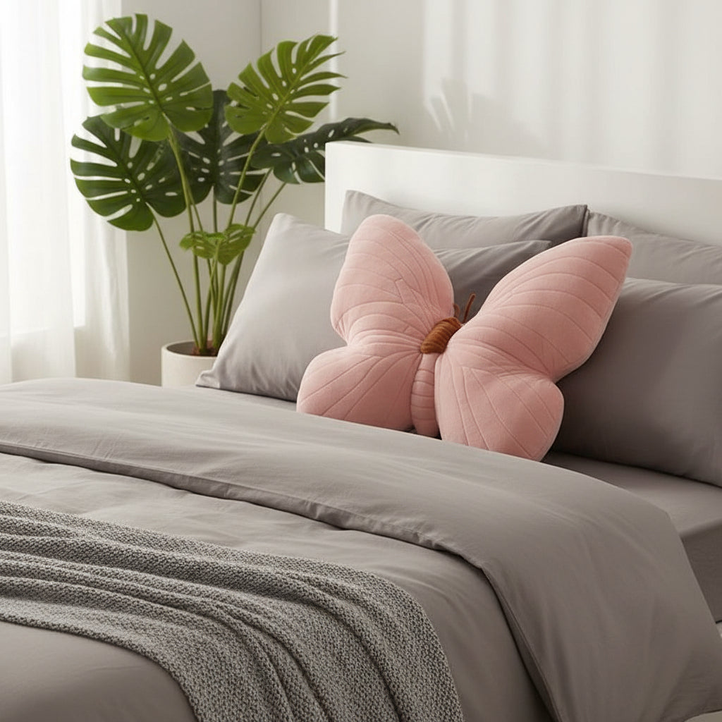 Bed with pink butterfly-shaped pillow and gray bedding, plant in the background