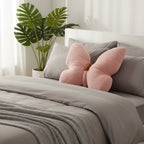 Bed with pink butterfly-shaped pillow and gray bedding, plant in the background