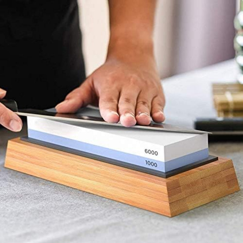 Person sharpening a knife on a whetstone with a wooden base.