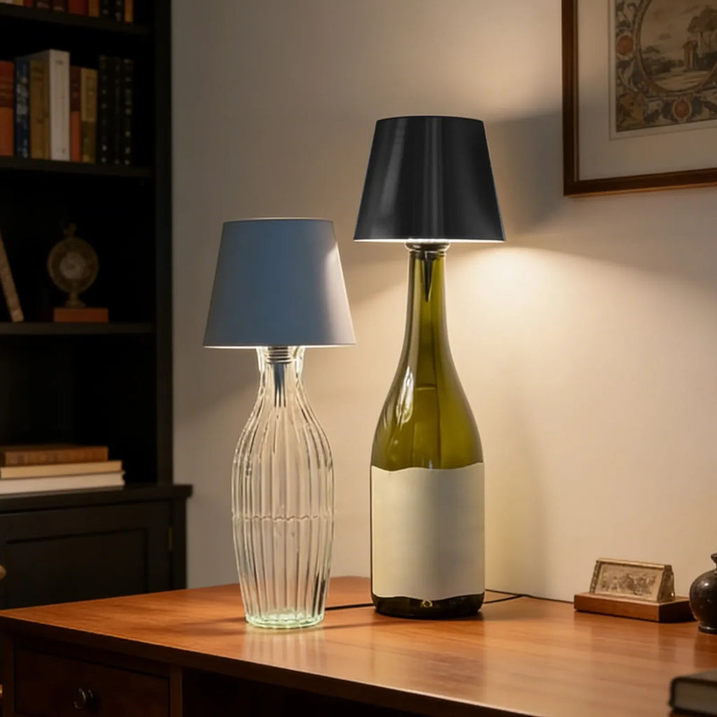 Two table lamps, one made from a clear glass bottle and the other from a green wine bottle, on a wooden surface.