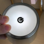 Round device with a power symbol on a white background, held by a hand.