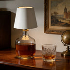 Lamp with a glass base containing a liquid, next to a glass of the same liquid on a wooden surface.