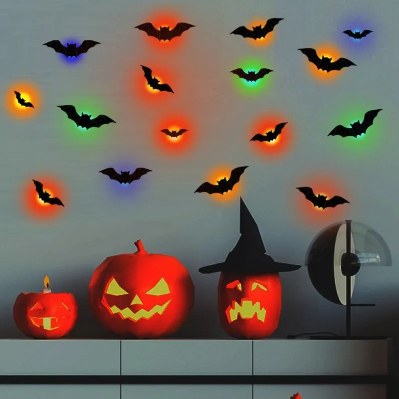 Halloween wall decals featuring black bat silhouettes that glow with multicolor light effects, displayed on a gray wall above carved jack-o'-lantern pumpkins and a black witch hat decoration.