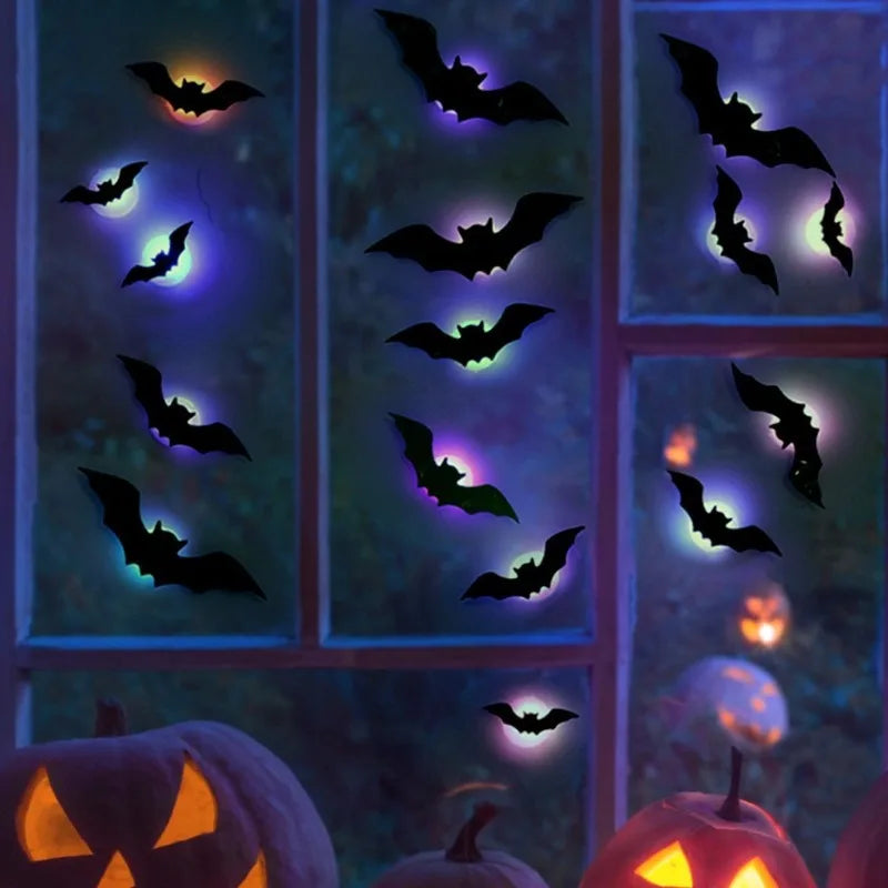 Halloween window decals featuring black bat silhouettes glowing with purple, blue, and orange light effects, shown applied to window panes above carved pumpkins.