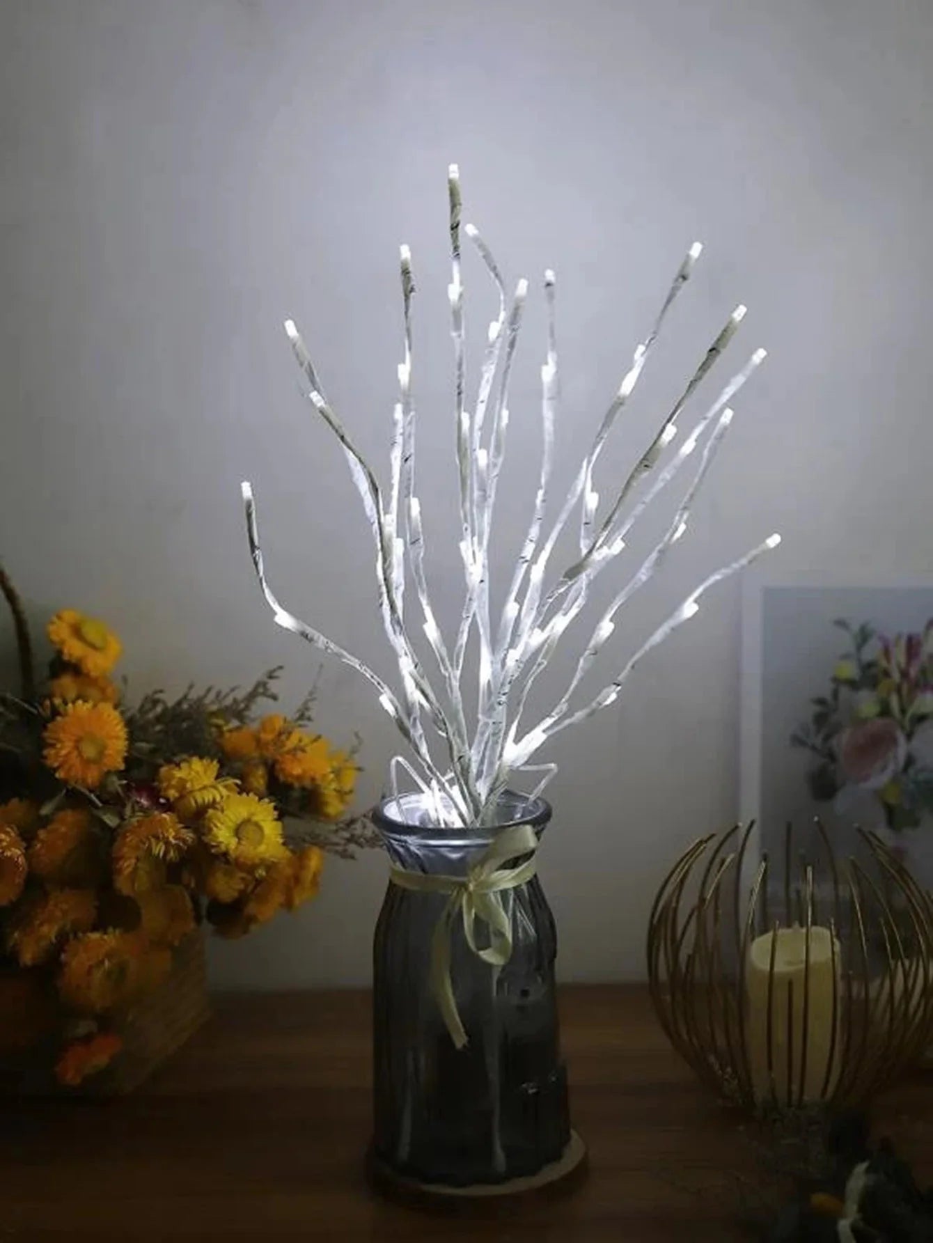 Decorative LED branch in a bottle with flowers and candle in the background