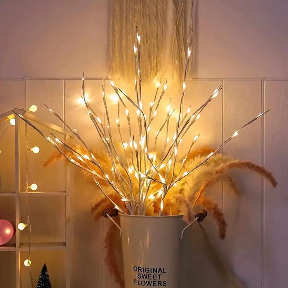 Decorative arrangement with LED lights in a white container labeled 'Original Sweet Flowers' against a neutral wall.