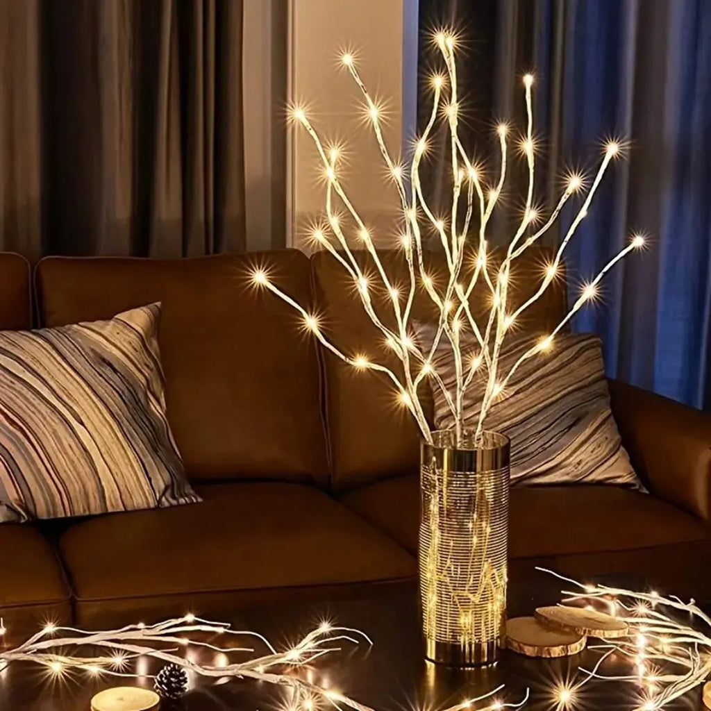 Decorative LED branch lights in a vase on a coffee table with a brown couch and striped pillows in the background.