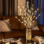 Decorative LED branch lights in a vase on a coffee table with a brown couch and striped pillows in the background.