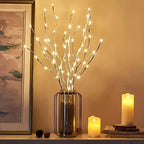 Decorative setup with lit branches in a vase on a shelf, candles, and a framed picture.