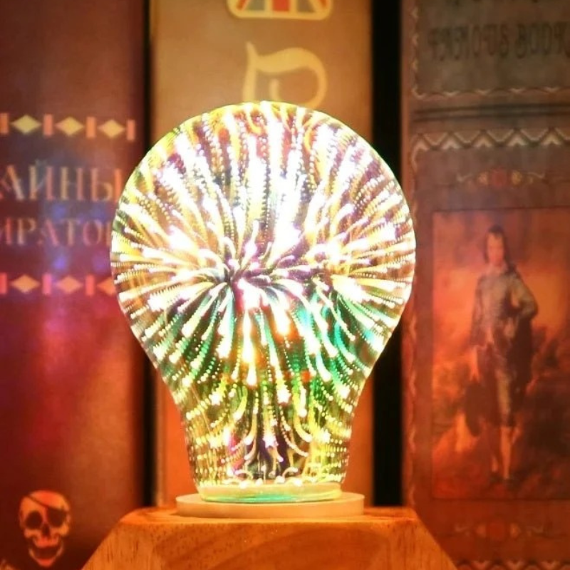 A decorative light bulb-shaped lamp glowing with multicolored fireworks patterns, displayed on a wooden stand against a dark, atmospheric background with vintage book illustrations.
