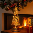 Decorative Christmas tree with lights on a table in front of a fireplace.