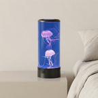 A cylindrical LED jellyfish aquarium lamp with a blue water-filled body and glowing pink jellyfish, placed on a bedside table next to a bed.