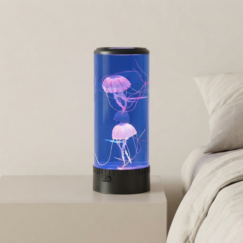 A cylindrical LED jellyfish aquarium lamp with a blue water-filled body and glowing pink jellyfish, placed on a bedside table next to a bed.
