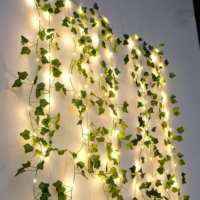 Artificial green ivy leaves with string lights on a white wall