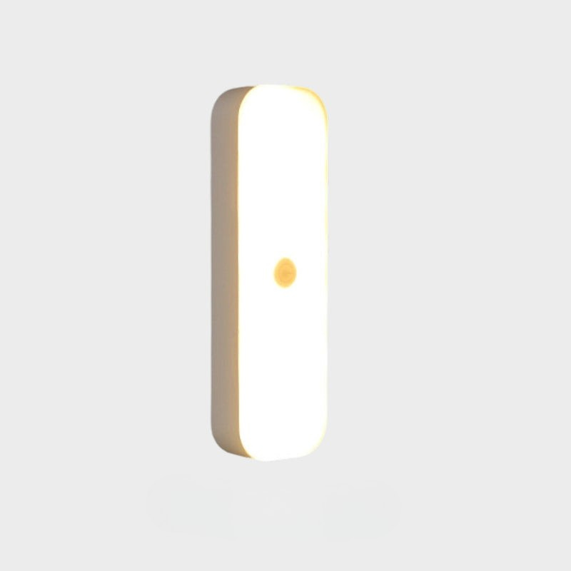 A modern, minimalist vertical rectangular wall light with rounded corners, featuring a warm white illuminated face and a small central gold accent, shown against a solid light gray background.