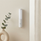 White cylindrical device mounted on a beige wall next to a vase with green leaves.