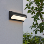 Modern outdoor wall light fixture on a gray wall with greenery in the background