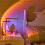 Room interior with a bed and nightstand, illuminated by a rainbow light effect.