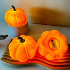 Three orange pumpkin-shaped lamps on a wooden stand with a plain background.