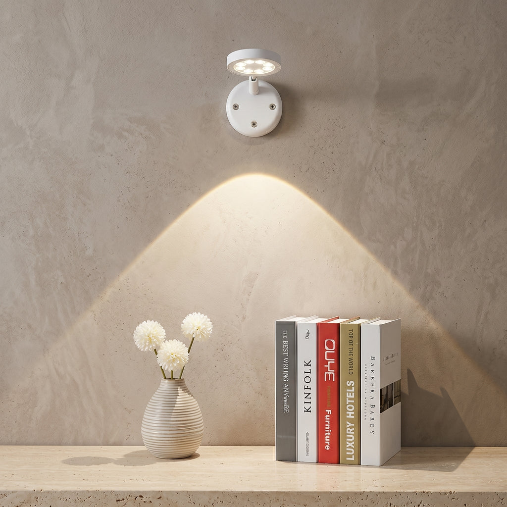 Wall-mounted light fixture casting a warm glow on a shelf with books and a vase.