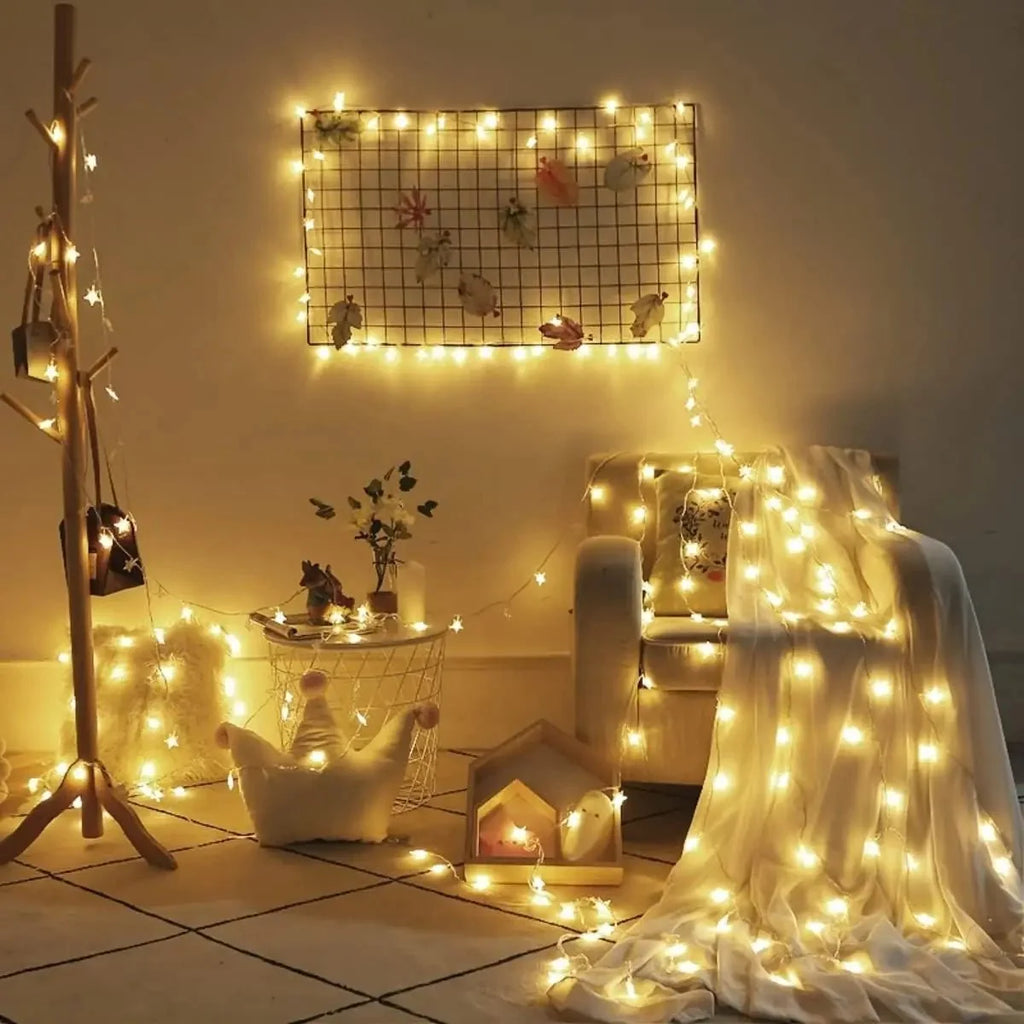 Warm white LED string lights draped over a cream armchair, a wooden coat rack, and a wire grid wall hanging in a cozy styled room scene.