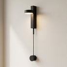 Modern black wall lamp with a cable extension on a light beige wall.