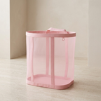 Pink mesh laundry basket on a light wooden floor with a neutral wall background