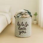 Laundry basket with clothes inside, placed on a wooden floor in a room.