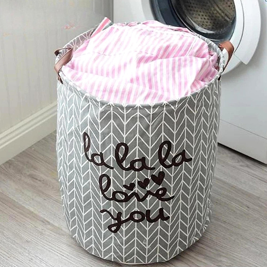 Gray laundry basket with pink fabric inside, placed in front of a washing machine.