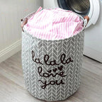 Gray laundry basket with pink fabric inside, placed in front of a washing machine.