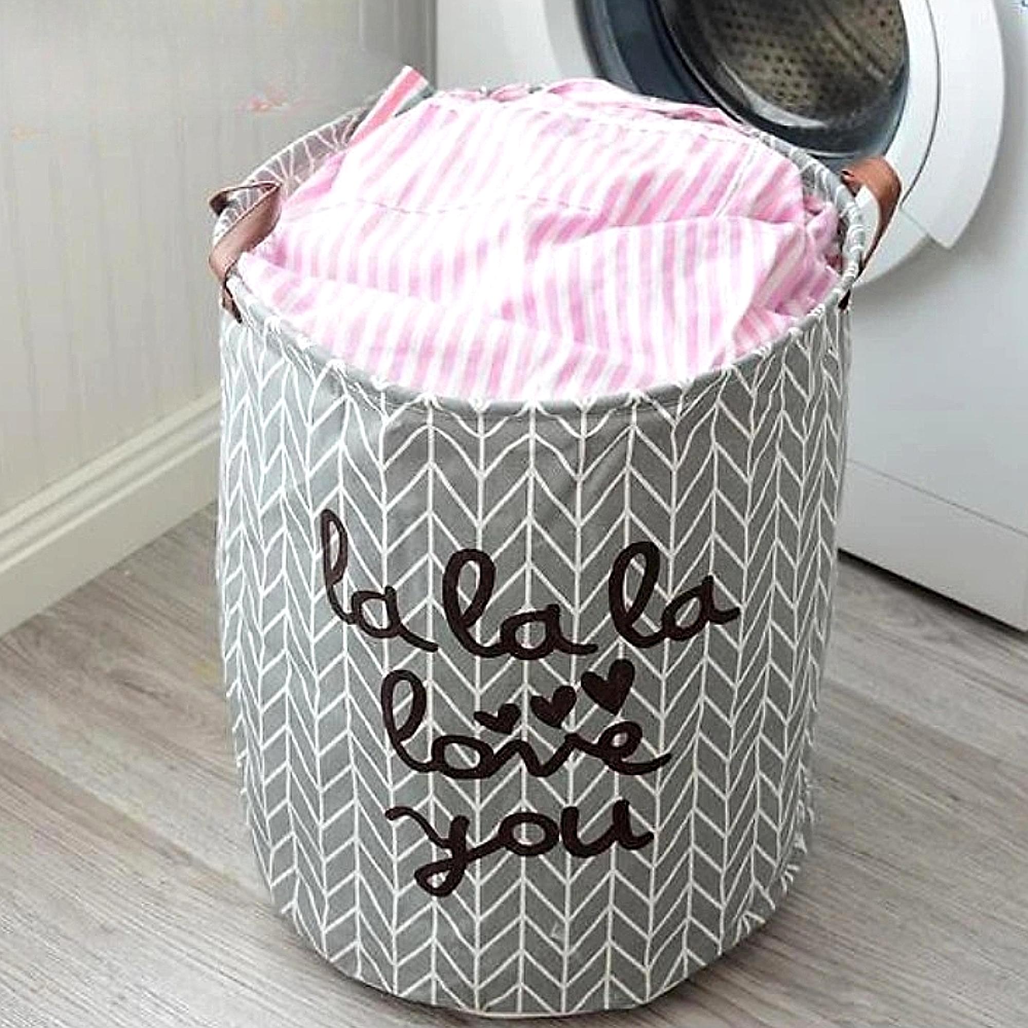 Gray laundry basket with pink fabric inside, placed in front of a washing machine.