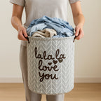 Person holding a laundry basket with clothes and 'lala la love you' text.