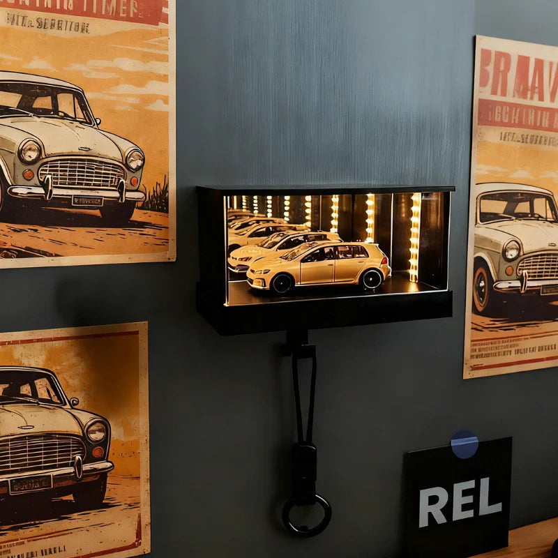Wall-mounted display case with illuminated cars, framed by vintage car posters on a dark wall.