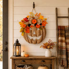 An autumn-themed burlap jack-o'-lantern wall hanging decorated with orange and yellow flowers, faux leaves, and a large burlap bow, displayed on a cream shiplap wall above a rustic wooden console table with seasonal decor.