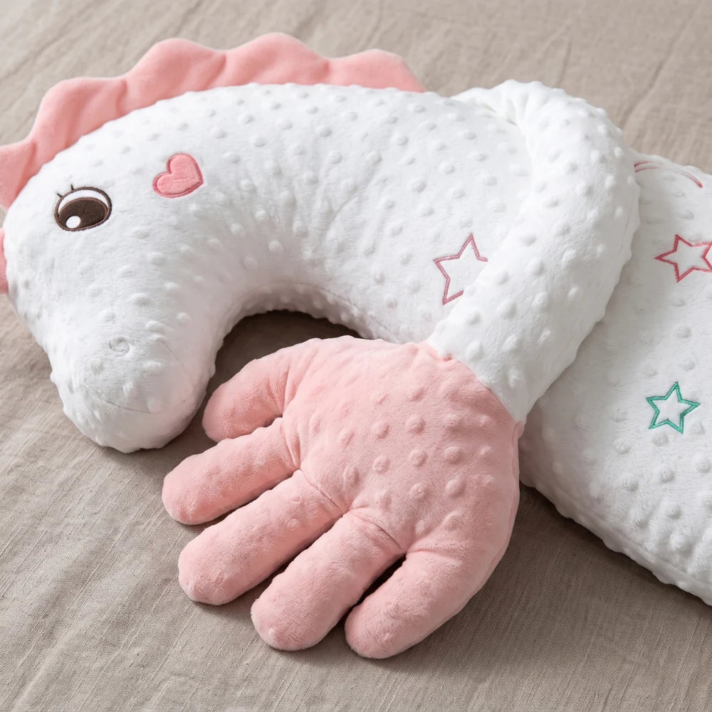 A plush dinosaur-shaped baby support pillow in white and pink with a textured dotty fabric, resting on a beige fabric surface.