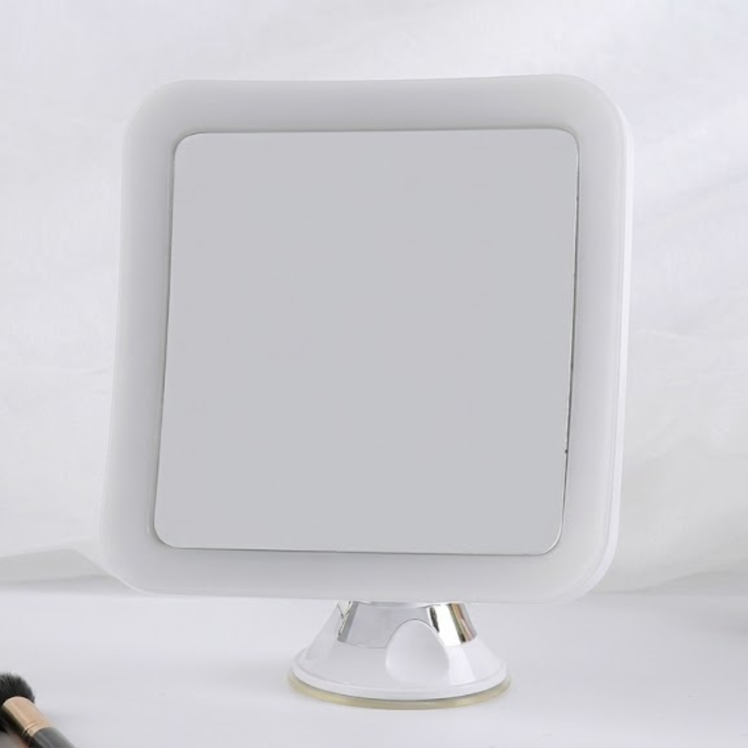 A square white vanity mirror with rounded corners and a chrome stand, shown against a white fabric backdrop.