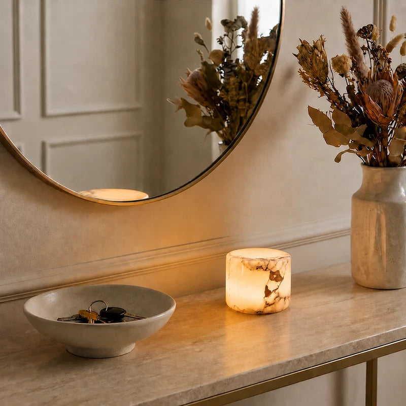 Round mirror on a table with a candle, vase of flowers, and bowl with keys.