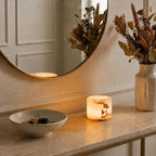 Round mirror on a table with a candle, vase of flowers, and bowl with keys.