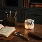 Desk setup with open book, magnifying glass, and decorative candle in a dimly lit room.