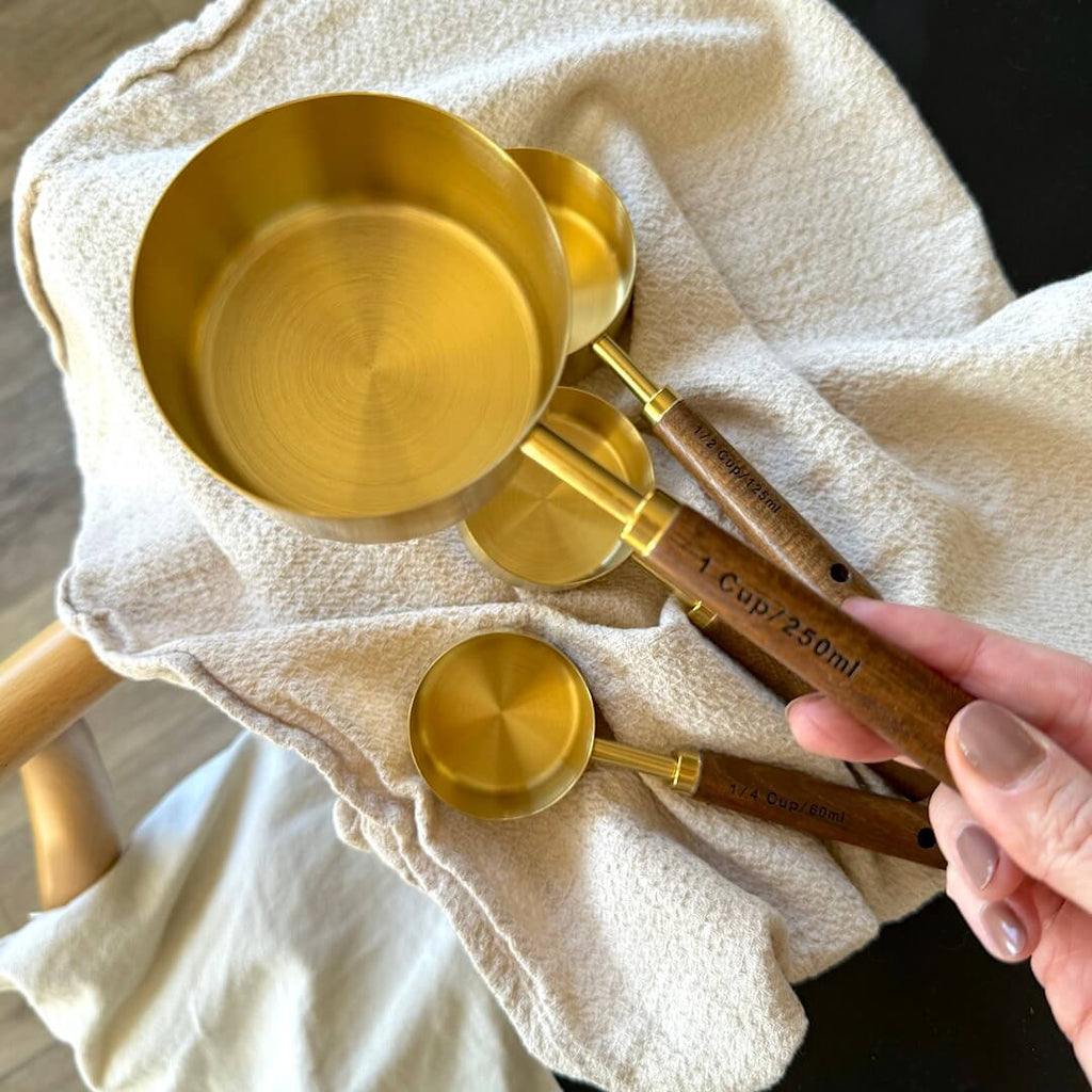 Set of gold measuring cups and spoons on a white cloth with a hand holding one of the spoons.