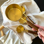 Set of gold measuring cups and spoons on a white cloth with a hand holding one of the spoons.