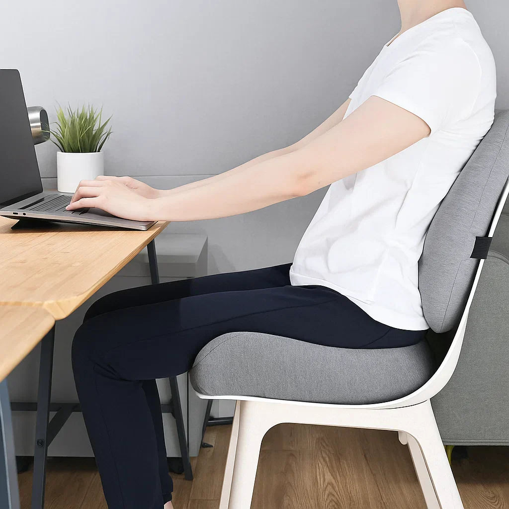 Person sitting at a desk with a laptop, using a backrest cushion.