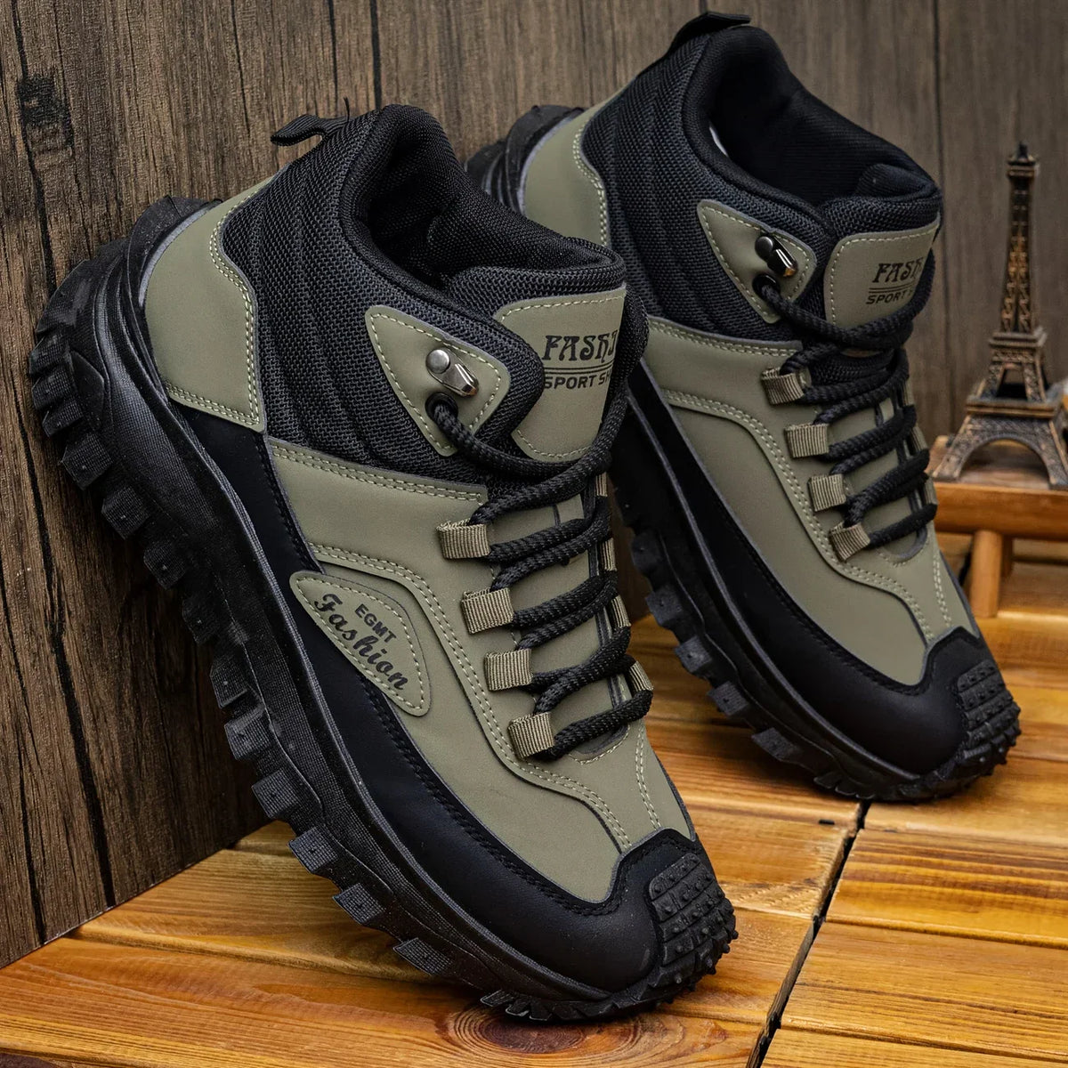 Pair of green and black hiking boots on a wooden surface with a wooden wall background.