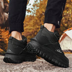 Black hiking boots with a textured sole worn by a person in an outdoor setting.