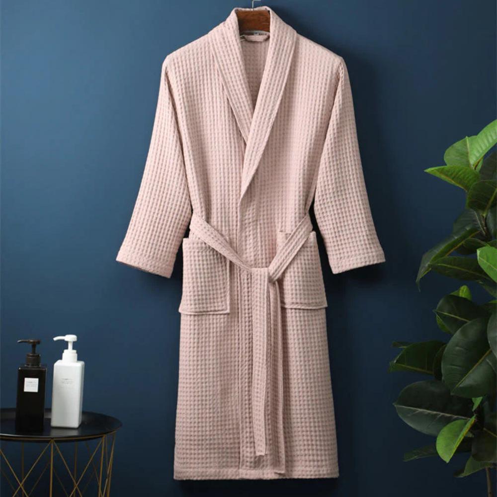 Pink checkered robe hanging against a blue wall with a plant and bottles on a table.