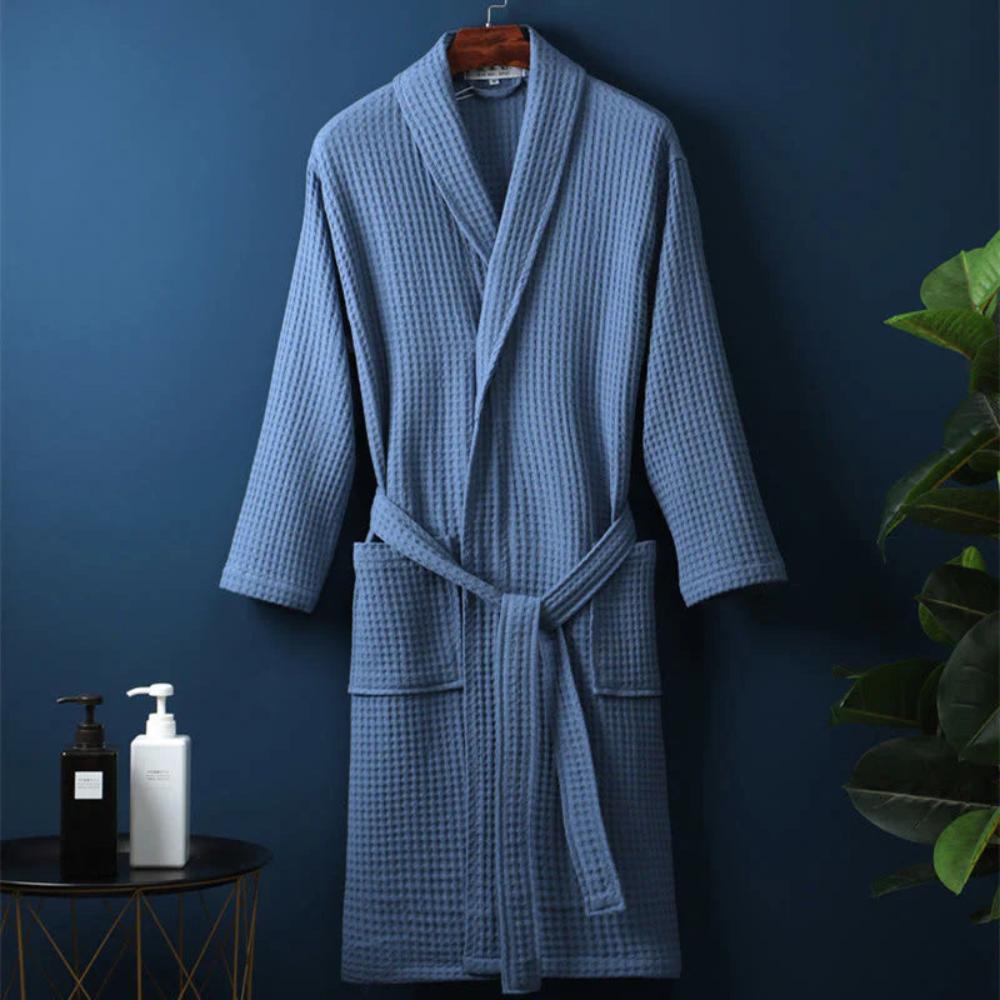 Blue checkered robe hanging on a dark blue wall with a plant and small table in the background.