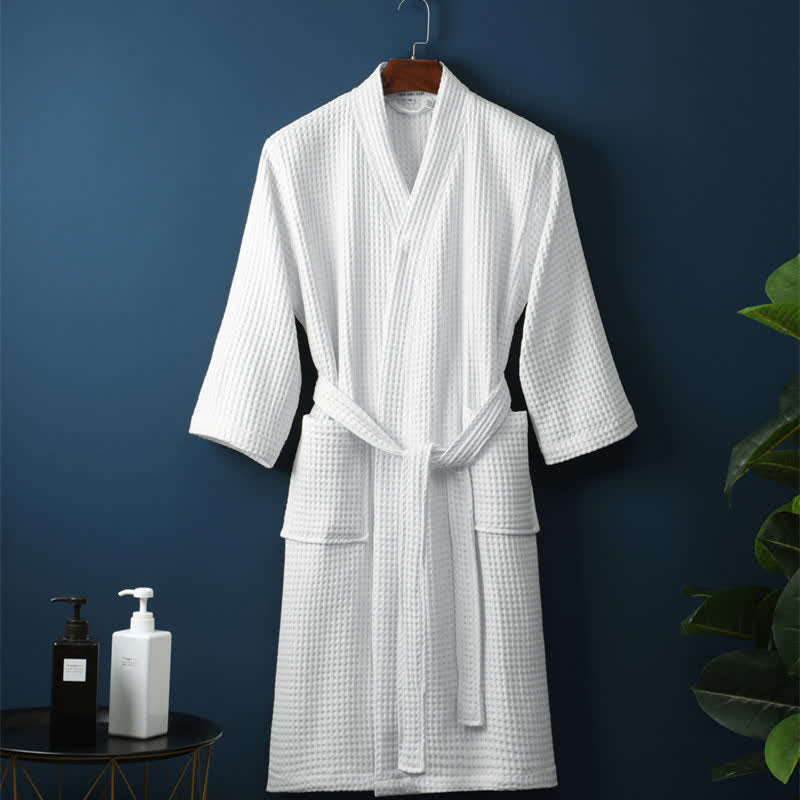White bathrobe hanging on a hook against a dark blue wall with a plant and small table in the foreground.