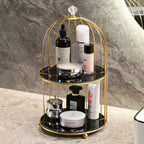 Gold birdcage-style organizer with beauty products on a marble surface.