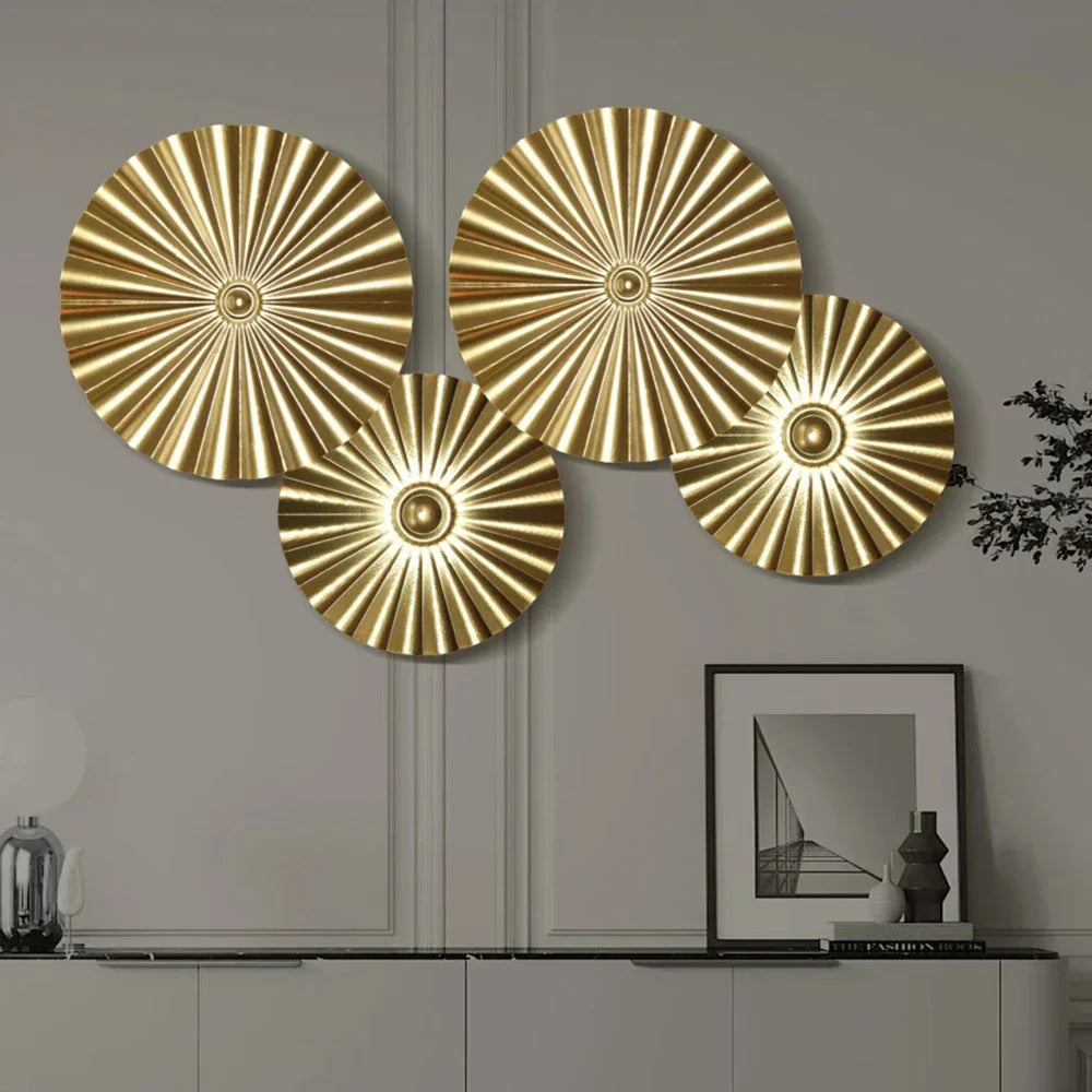 Set of four gold decorative wall plates on a neutral wall with a framed picture and lamp.